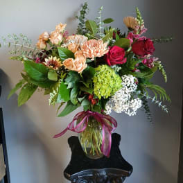 Mixed bouquet of roses, chrysanthemums, and hydrangea in a glass vase with a ribbon
