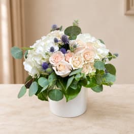 White and blush roses with purple accents in a white vase