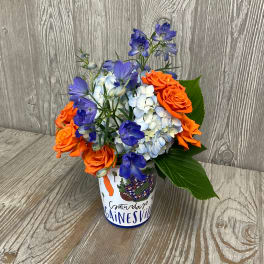 Orange roses and blue flowers arranged in a decorated cup