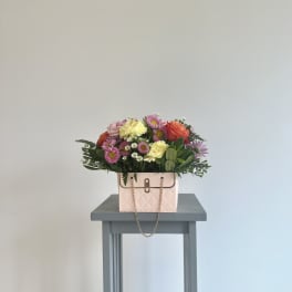 Mixed bouquet in a pink handbag-style container on a small table