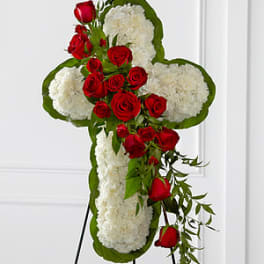 Cross-shaped floral tribute with red roses and white flowers on an easel