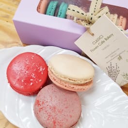 Assorted macarons on a white plate beside a lavender gift box with ribboned tag
