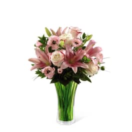 Pink lilies and roses arranged in a tall green glass vase