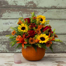 Autumn bouquet in a pumpkin container with sunflowers, roses, lilies, and mums