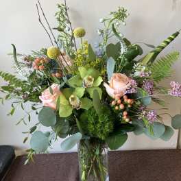 Tall mixed bouquet in a clear glass vase with pink roses and green orchids