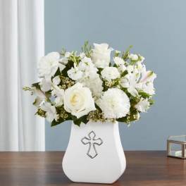 White floral arrangement in a white vase with a cross emblem