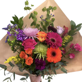 Colorful mixed bouquet with roses, gerberas, and purple blooms in brown paper