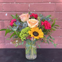 Mixed bouquet with roses, sunflower, and pink carnations in a glass vase