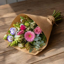 Hand-tied bouquet of pink, white, and purple flowers in brown paper