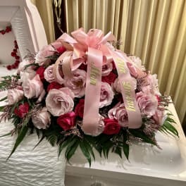 Pink and red rose arrangement on a white casket with a pink ribbon.