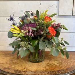 Mixed bouquet in a glass vase with orange roses, yellow blooms, and purple flowers