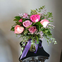 Pink and lavender roses arranged in a glass vase with a purple ribbon.