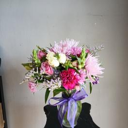 Pink and white mixed bouquet in a glass vase with a purple ribbon