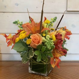 Orange roses and lilies in a square glass vase with autumn leaves