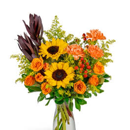 Bouquet of sunflowers, orange roses, and carnations in a clear glass vase