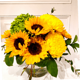 Yellow sunflowers and mums arranged in a clear glass vase