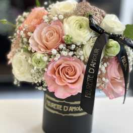 Pink and white roses arranged in a black hatbox with ribbon