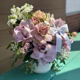 Pink and lavender rose bouquet in a white vase with a ribbon