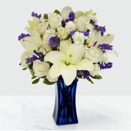 White lilies and roses with purple filler in a blue glass vase