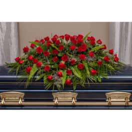 Red rose casket spray with greenery on a dark casket