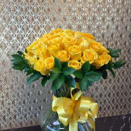 Yellow rose bouquet in a clear glass vase with a yellow ribbon