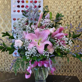 Pink lilies and roses in a glass vase with a pink ribbon