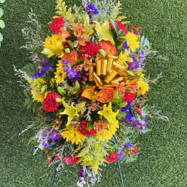 Colorful standing floral spray with a gold ribbon on a grassy background