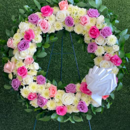 Circular floral wreath of pink, purple, and white roses with a white bow