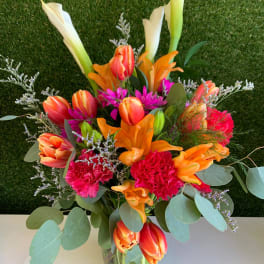 Bright mixed bouquet with calla lilies, tulips, carnations, and lilies in a glass vase
