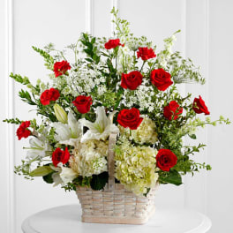 Basket arrangement of red roses, white lilies, and pale hydrangeas