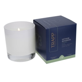 White candle in a glass tumbler beside a navy candle box