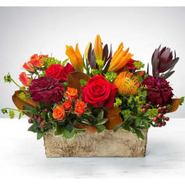 Mixed bouquet in a rustic rectangular container with red, orange, and burgundy flowers