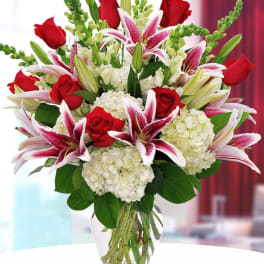 Bouquet of red roses, pink lilies, and white hydrangeas in a glass vase