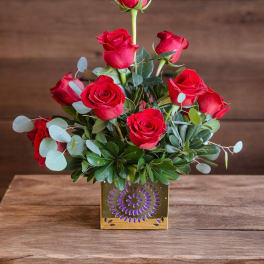 Red roses arranged in a gold square vase with eucalyptus accents