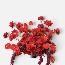 Red floral arrangement with roses and anthuriums in a dark vase