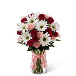 Bouquet of red roses, pink carnations, and white daisies in a glass vase