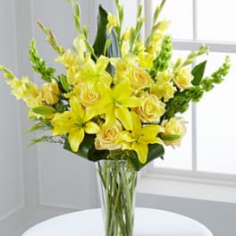 Yellow lilies and roses arranged in a clear glass vase