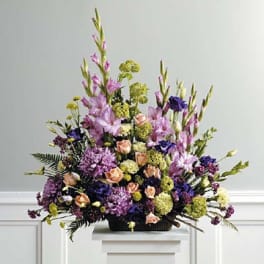 Tall fan-shaped arrangement of purple, peach, and green flowers in a dark basket