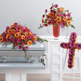 Bright gerbera daisy funeral arrangements on a casket and easel cross.