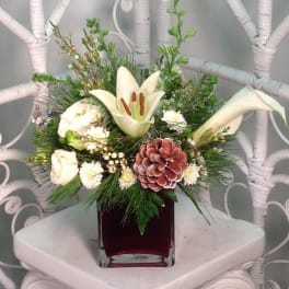 White lilies and roses in a red glass vase with pine accents