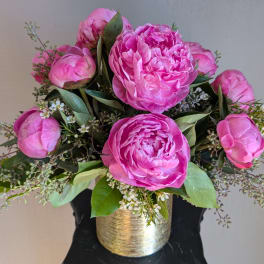Pink peonies arranged in a gold vase with small white filler flowers