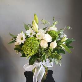 White and green floral arrangement in a glass vase with a white ribbon