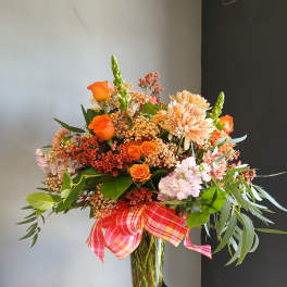 Orange and blush mixed bouquet in a clear glass vase with a plaid ribbon