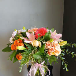 Mixed bouquet of pink lilies, orange roses, and a red gerbera in a glass vase