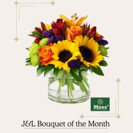 Mixed bouquet of sunflowers, roses, and lilies in a clear glass vase