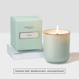 Lit scented candle beside its mint-green box