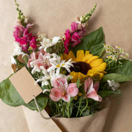 Bouquet of sunflowers, pink alstroemeria, and white daisies in kraft paper