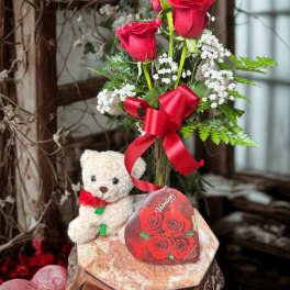 Red roses in a glass vase with a teddy bear and red ribbon