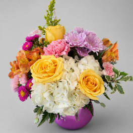 Colorful bouquet of yellow roses, hydrangeas, and mixed blooms in a purple vase