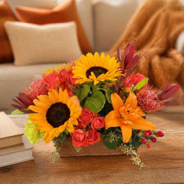 Mixed bouquet with sunflowers, orange lilies, and red roses in a low wooden container